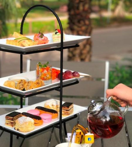 Luxury high tea service at J7 Hotel Siem Reap, showing a three-tier stand filled with pastries, macarons, savory snacks, and hot tea being poured.