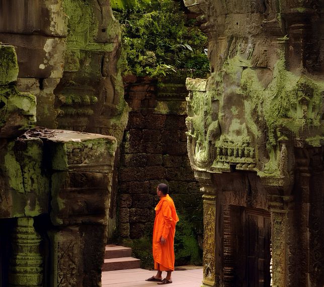 Buddhist monk in saffron robes walking through ancient stone temple ruins near J7 Hotel Siem Reap.