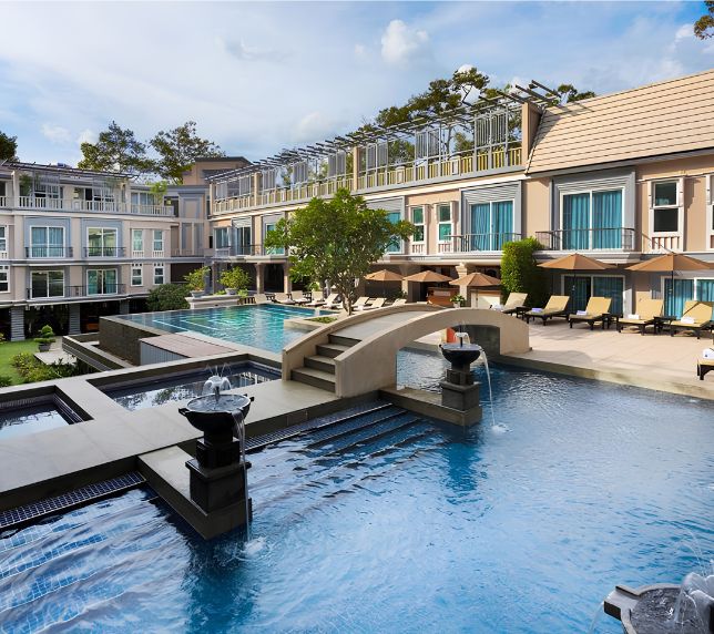 Luxury outdoor swimming pool with a stone bridge, water fountains, and sun loungers at J7 Angkor Hotel in Siem Reap, Cambodia.